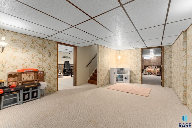 finished basement featuring a paneled ceiling, carpet, stairs, and wallpapered walls