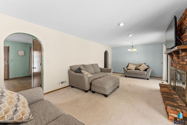 living area with an inviting chandelier, a brick fireplace, light colored carpet, and arched walkways