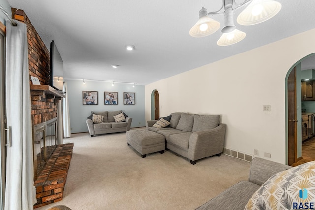 carpeted living room with visible vents, arched walkways, a brick fireplace, and track lighting