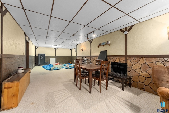 carpeted dining area with a paneled ceiling, a textured wall, and wainscoting