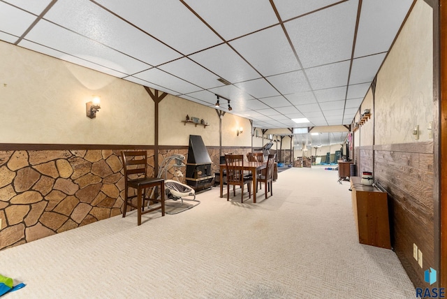 carpeted dining area featuring a drop ceiling, wainscoting, and a wood stove