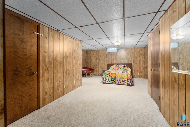 carpeted bedroom featuring a paneled ceiling and wood walls