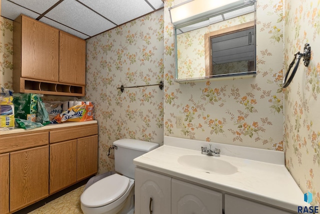 bathroom with a drop ceiling, toilet, vanity, and wallpapered walls