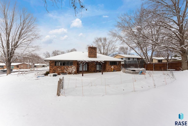 snow covered property featuring a chimney and fence