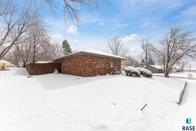 view of snowy exterior featuring brick siding and fence