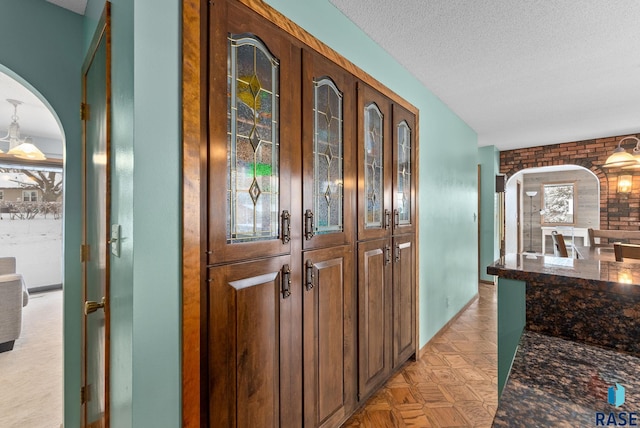 hallway with arched walkways, brick wall, and a textured ceiling