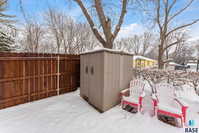 snow covered structure featuring an outbuilding, a storage shed, and fence