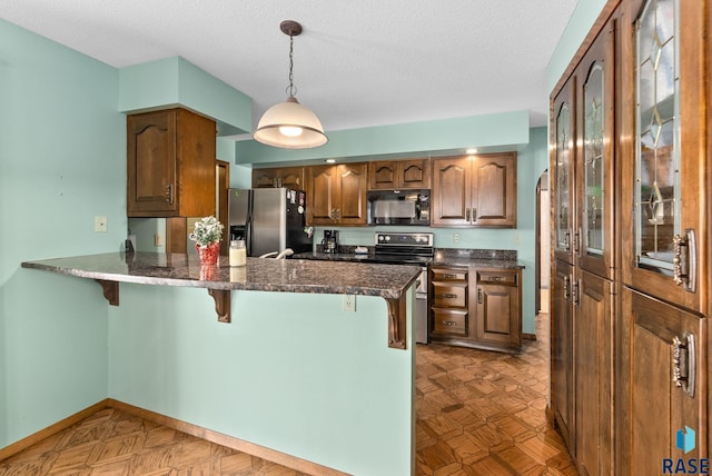 kitchen with baseboards, a peninsula, appliances with stainless steel finishes, pendant lighting, and a kitchen bar