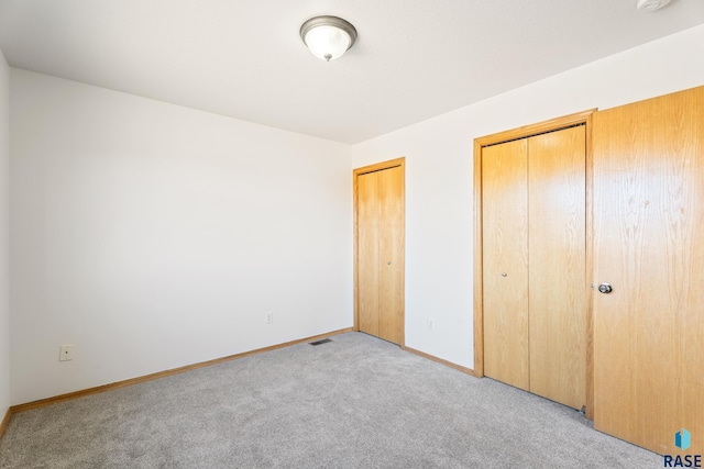 unfurnished bedroom with two closets, visible vents, baseboards, and light colored carpet