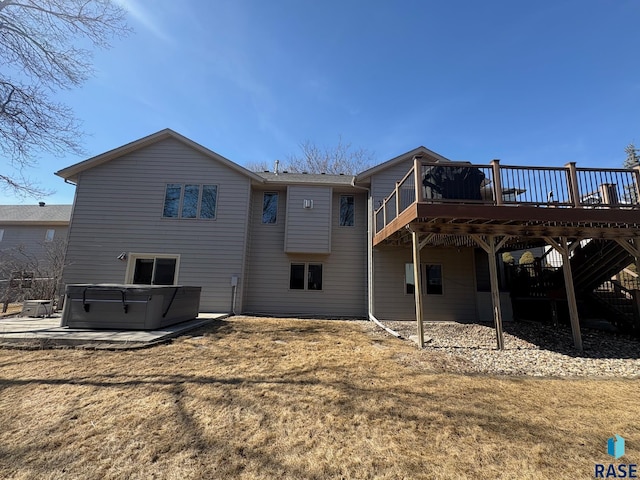 rear view of property with a wooden deck, a lawn, a patio area, and a hot tub