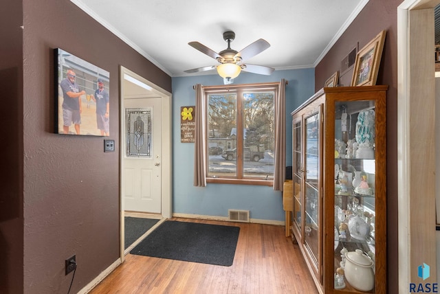 doorway to outside with visible vents, baseboards, wood finished floors, and crown molding