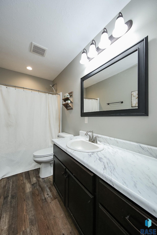 bathroom with visible vents, toilet, vanity, wood finished floors, and a textured ceiling