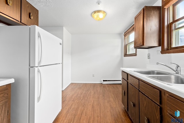 kitchen featuring wood finished floors, freestanding refrigerator, a sink, light countertops, and a baseboard heating unit