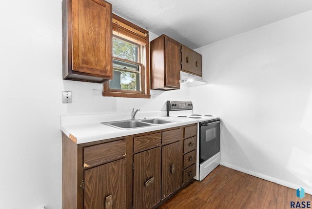 kitchen with a sink, under cabinet range hood, range with electric stovetop, baseboards, and dark wood-style flooring