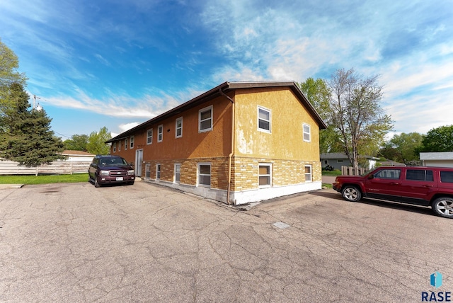 view of side of property with stucco siding, brick siding, and fence