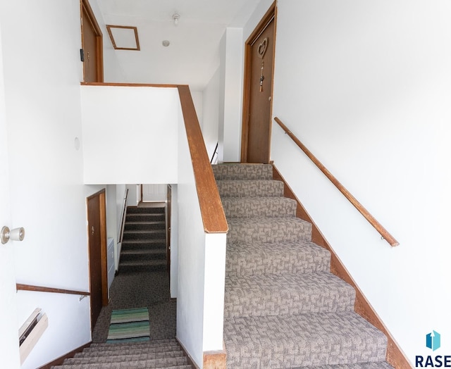 stairway with a baseboard heating unit and carpet