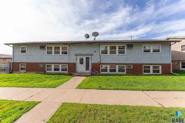 bi-level home with stucco siding, brick siding, a front yard, and a wall mounted AC