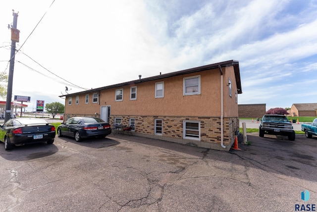 exterior space featuring stucco siding, brick siding, and uncovered parking