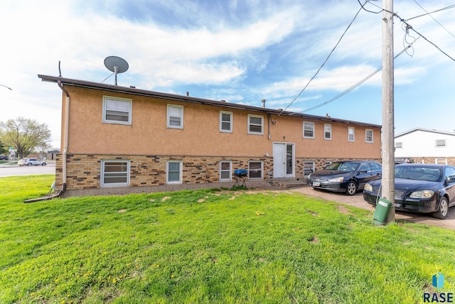 back of property featuring a yard, brick siding, and stucco siding