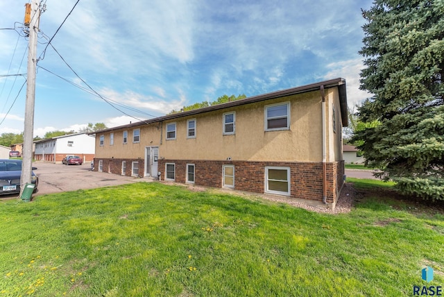 back of property featuring stucco siding, brick siding, and a lawn