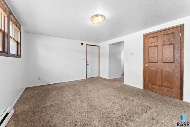 unfurnished room featuring a baseboard heating unit, baseboards, a textured ceiling, and carpet flooring