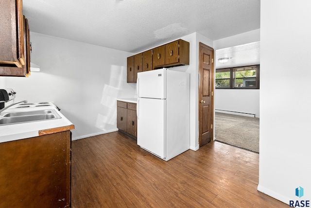 kitchen with a baseboard radiator, freestanding refrigerator, a sink, dark wood-type flooring, and light countertops