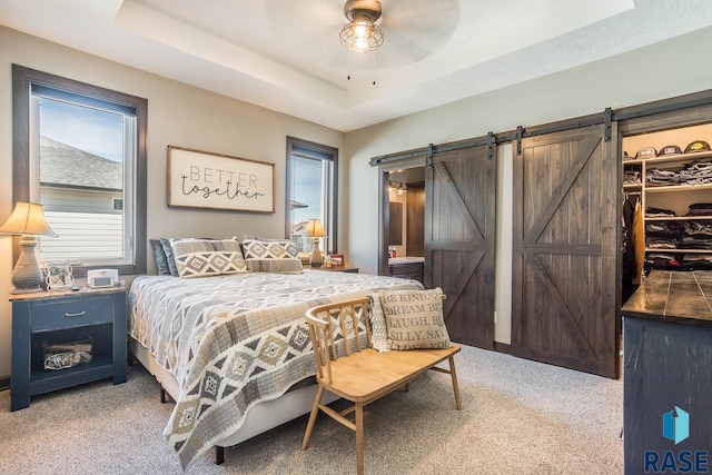 bedroom with a walk in closet, a barn door, light carpet, a closet, and a raised ceiling