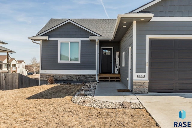 view of front of house with stone siding, an attached garage, a shingled roof, and fence