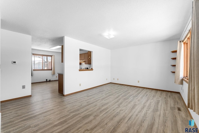 unfurnished living room featuring visible vents, a textured ceiling, baseboards, and wood finished floors