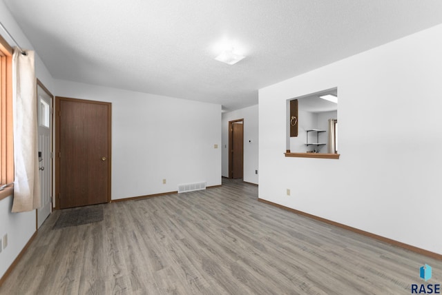 unfurnished room with visible vents, baseboards, a textured ceiling, and wood finished floors