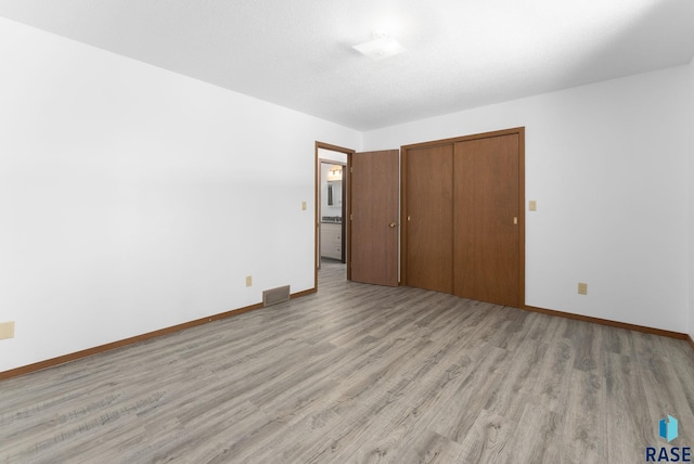 unfurnished bedroom with a closet, visible vents, light wood-type flooring, and baseboards