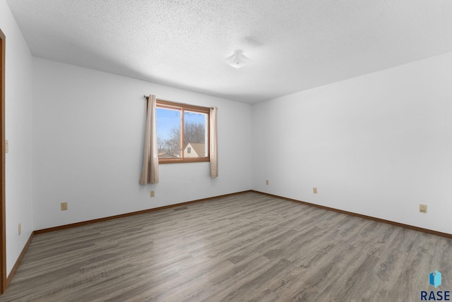 spare room featuring visible vents, baseboards, a textured ceiling, and wood finished floors