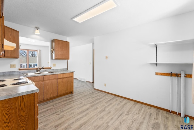 kitchen with visible vents, cooktop, brown cabinets, light wood-style floors, and a sink