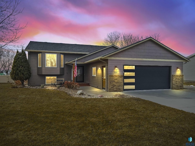 split level home featuring brick siding, a lawn, concrete driveway, and an attached garage