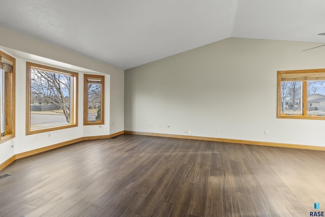 empty room featuring lofted ceiling, a healthy amount of sunlight, and dark wood-style floors