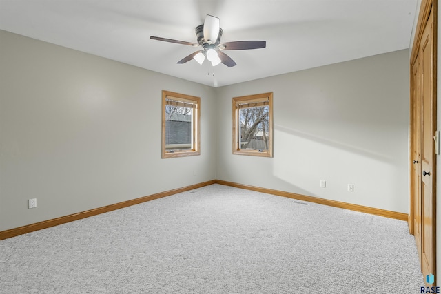 carpeted spare room featuring a ceiling fan and baseboards