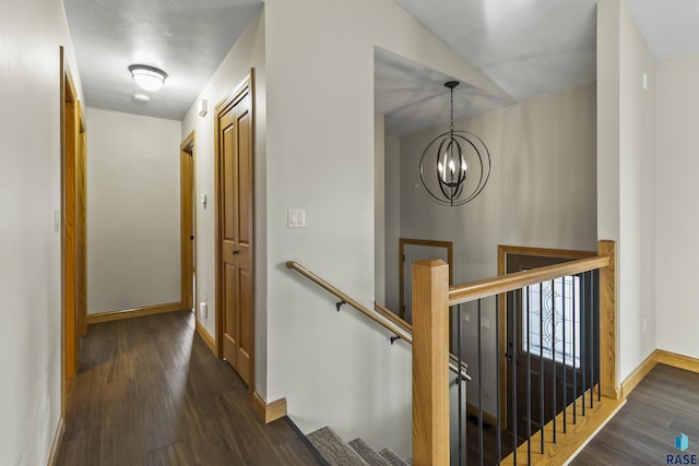 hallway with an upstairs landing, dark wood-style floors, baseboards, and a notable chandelier