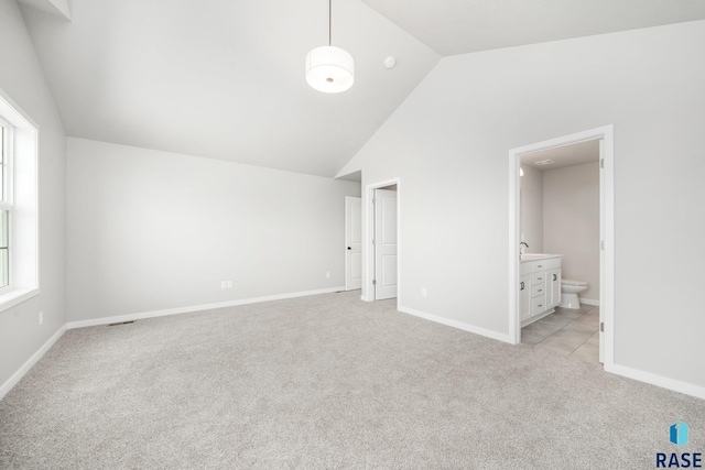 unfurnished bedroom with light colored carpet, high vaulted ceiling, ensuite bathroom, and baseboards