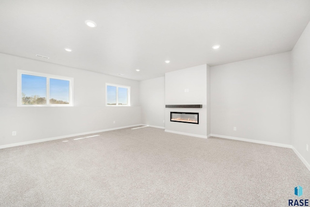 unfurnished living room featuring a glass covered fireplace, recessed lighting, baseboards, and light colored carpet