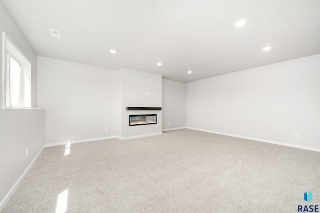 unfurnished living room with recessed lighting, baseboards, a glass covered fireplace, and carpet flooring