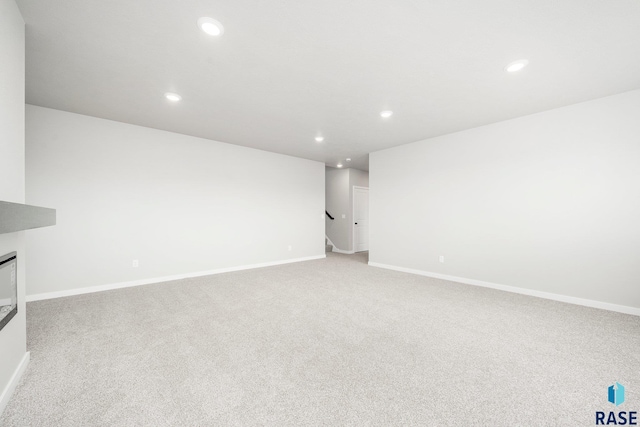 unfurnished living room with recessed lighting, baseboards, light colored carpet, and a glass covered fireplace