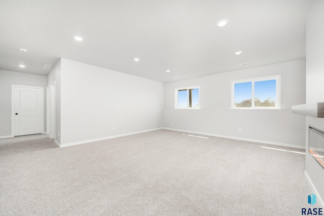 unfurnished living room with recessed lighting, baseboards, and light carpet