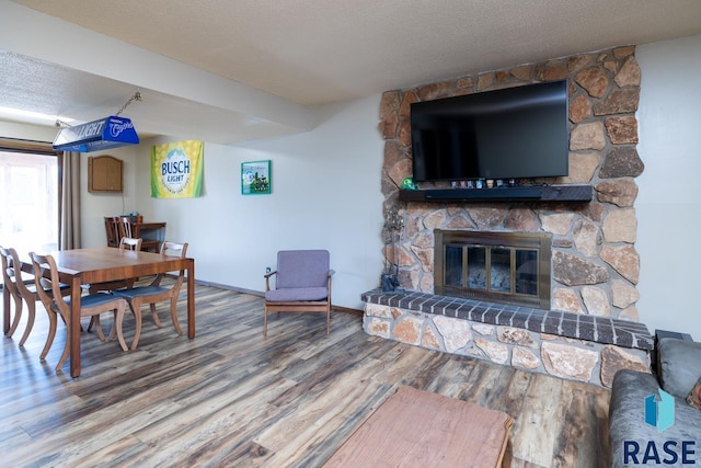 dining room with a stone fireplace, a textured ceiling, baseboards, and wood finished floors