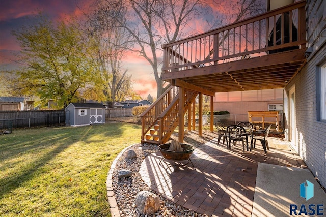 yard at dusk featuring a fire pit, a shed, a fenced backyard, a patio area, and an outbuilding