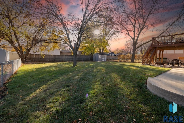 yard at dusk featuring a shed, a fenced backyard, stairs, an outdoor structure, and a deck