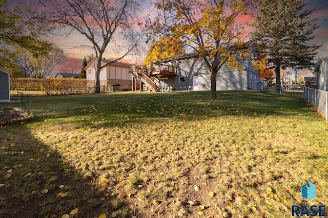 yard at dusk featuring a wooden deck, stairs, and fence