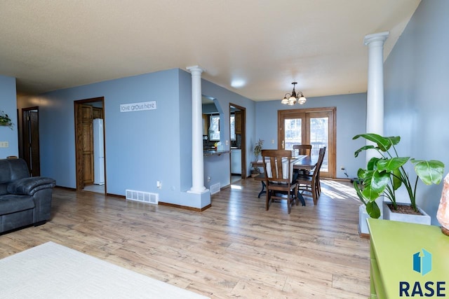 dining area featuring visible vents, light wood-style flooring, an inviting chandelier, baseboards, and ornate columns