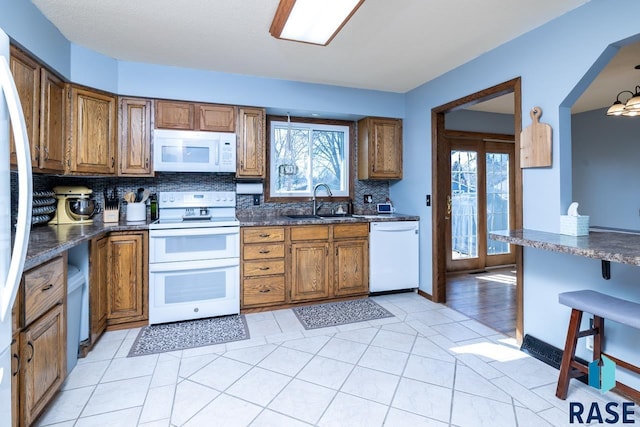 kitchen featuring tasteful backsplash, brown cabinetry, plenty of natural light, white appliances, and a sink