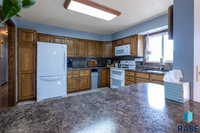 kitchen with a sink, dark countertops, tasteful backsplash, white appliances, and brown cabinetry