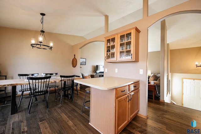 kitchen with dark wood-style floors, arched walkways, light countertops, glass insert cabinets, and a kitchen bar